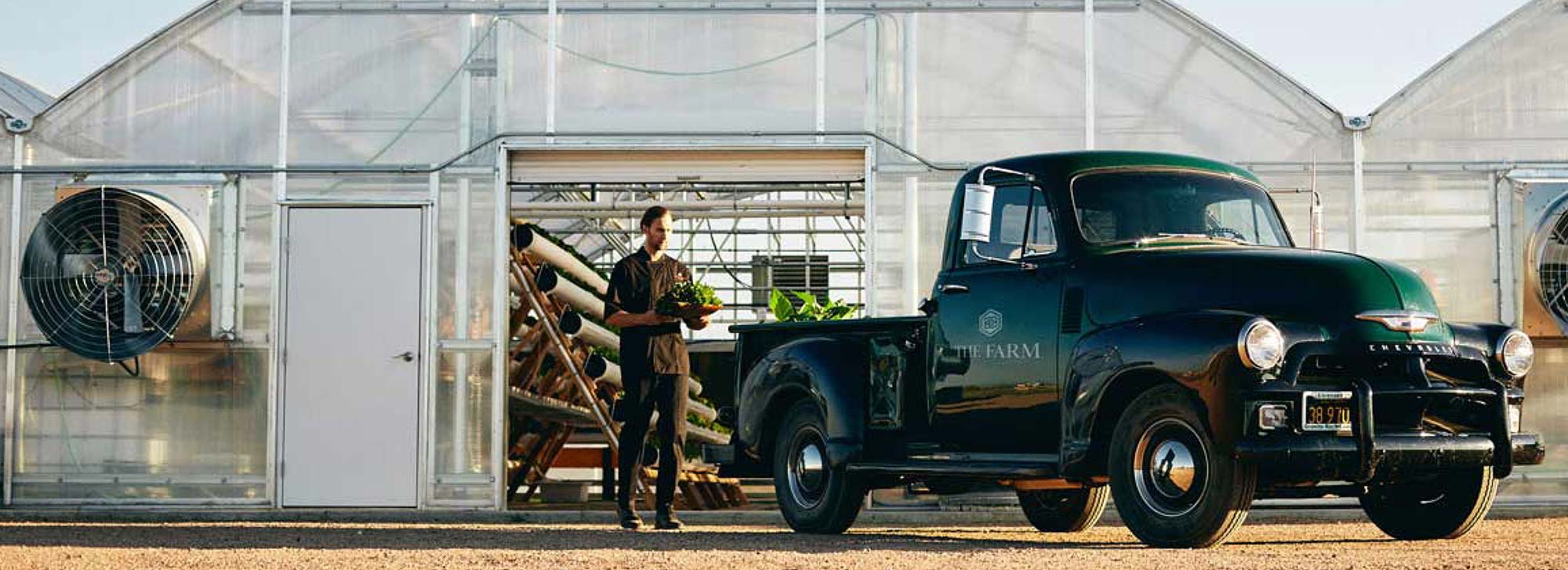 Serge Boon holding plants next to a truck outside of a greenhouse.